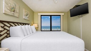 Habitación de hotel con una cama grande, televisión y vista a la playa.