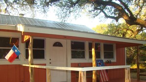 A wooden house with a porch, a flag, and a door. - Secluded, shady river front Get-away cabin (Uvalde)
