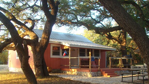 A rustic building with a red exterior, a stone foundation, and a metal roof. - Secluded, shady river front Get-away cabin (Uvalde)