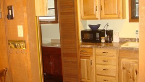 A kitchen with wooden cabinets, a microwave, and a sink. - Secluded, shady river front Get-away cabin (Uvalde)
