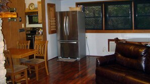 A spacious living room with a wooden ceiling and a large window. - Secluded, shady river front Get-away cabin (Uvalde)