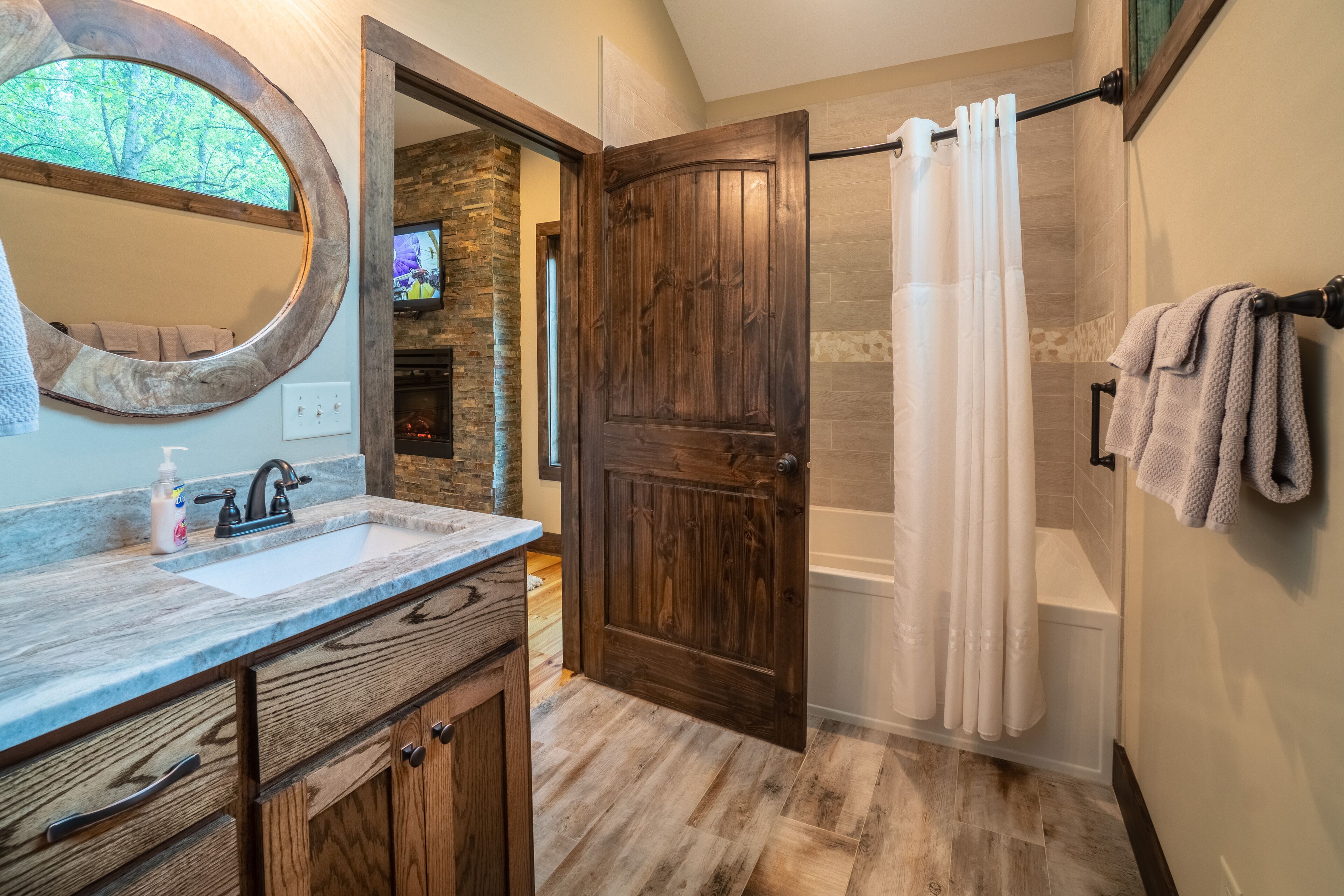 Une salle de bain avec une porte en bois, une baignoire, un rideau de douche et un lavabo avec un miroir.