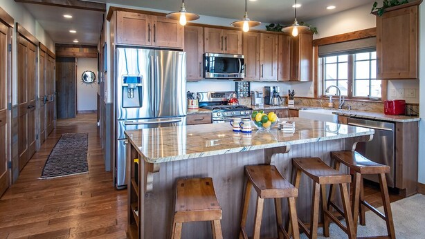 Una cocina moderna con armarios de madera, electrodomésticos de acero inoxidable y una isla de mármol con taburetes.