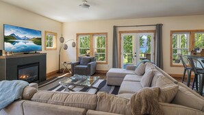 Ein Wohnzimmer mit Kamin, Fernseher, einer Couch und Blick auf einen See durch große Fenster.