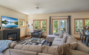 Ein Wohnzimmer mit Kamin, Fernseher, einer Couch und Blick auf einen See durch große Fenster.