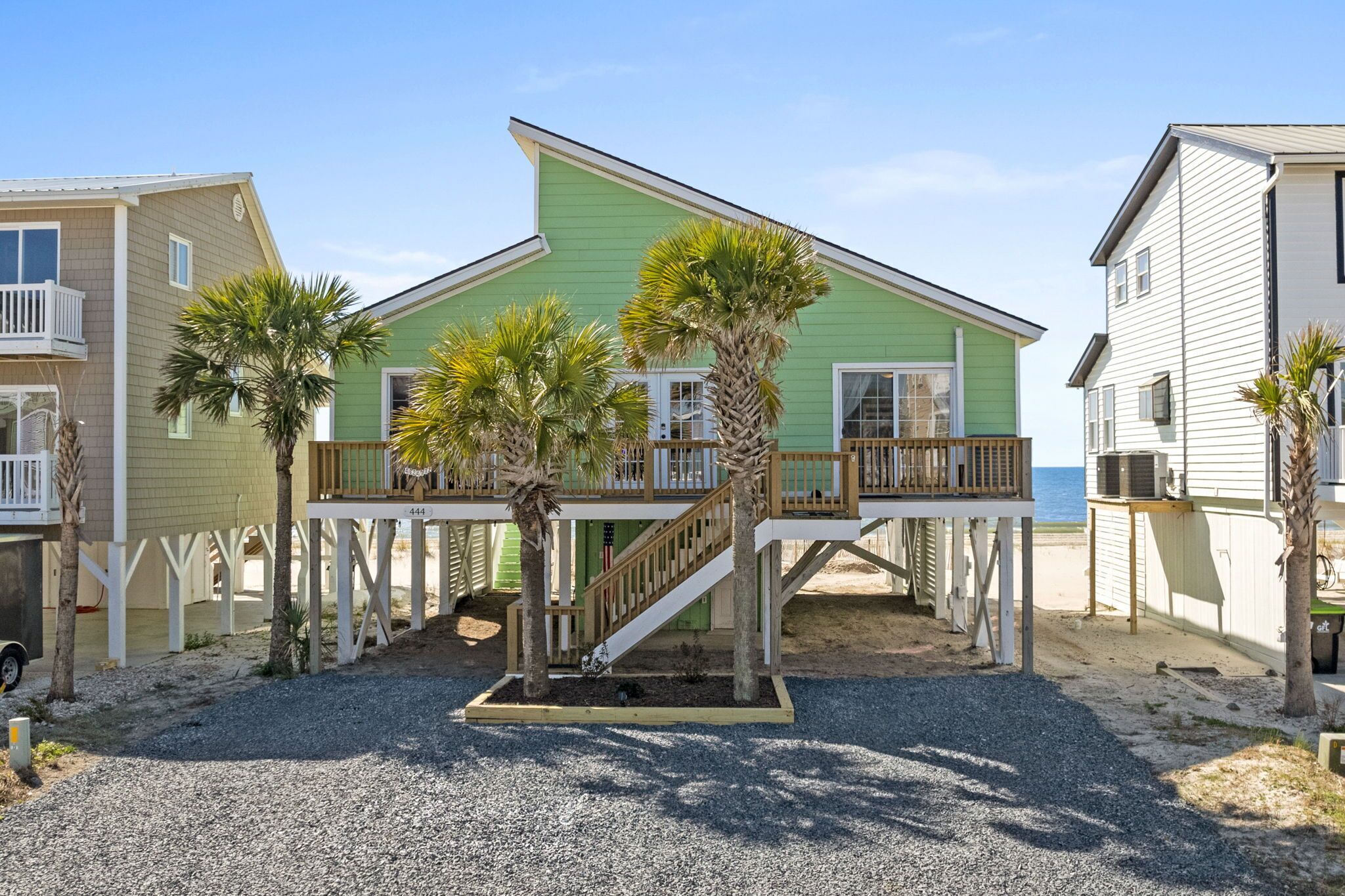 Une propriété située en bord de mer, avec une maison aux murs verdoyants, une terrasse en bois et des palmiers.
