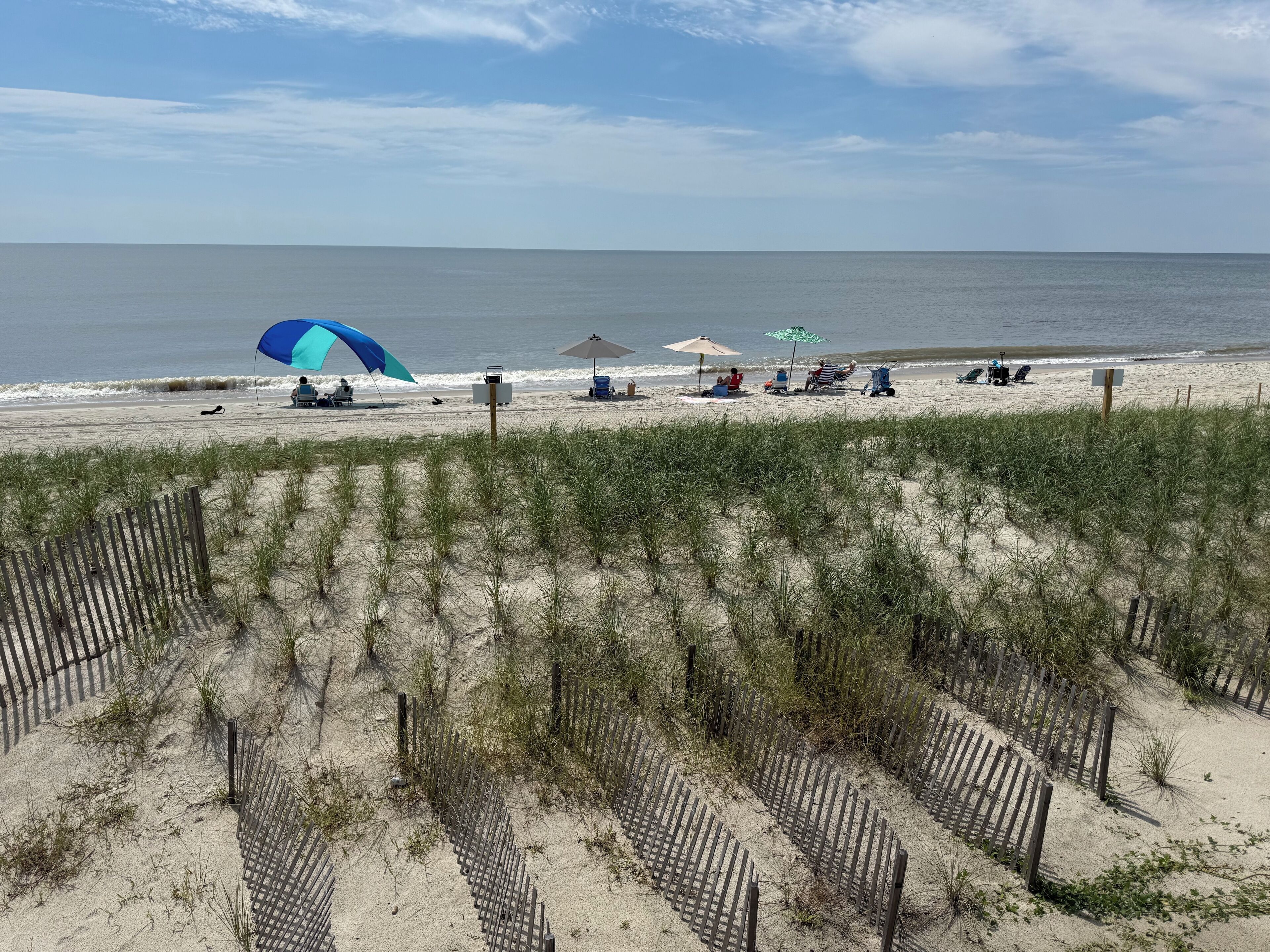 A beach with a wooden fence, beach chairs, umbrellas, and a lifeguard stand.