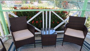 Een terras met twee rieten stoelen en een kleine tafel, omgeven door een witte balustrade en rode bloemen.