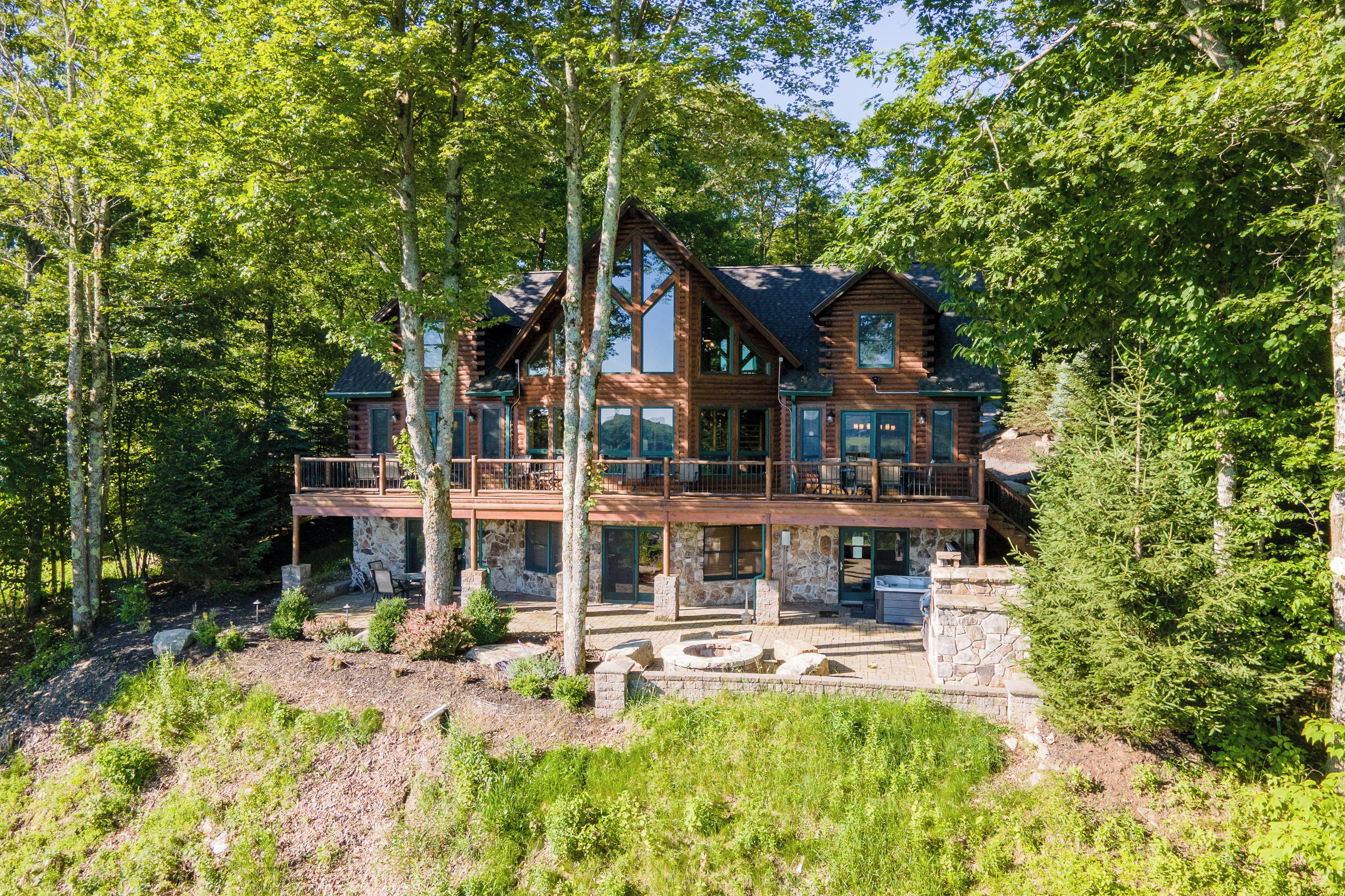 Une grande cabane en rondins dotée de plusieurs terrasses et reposant sur des fondations en pierre, entourée d’une forêt dense.