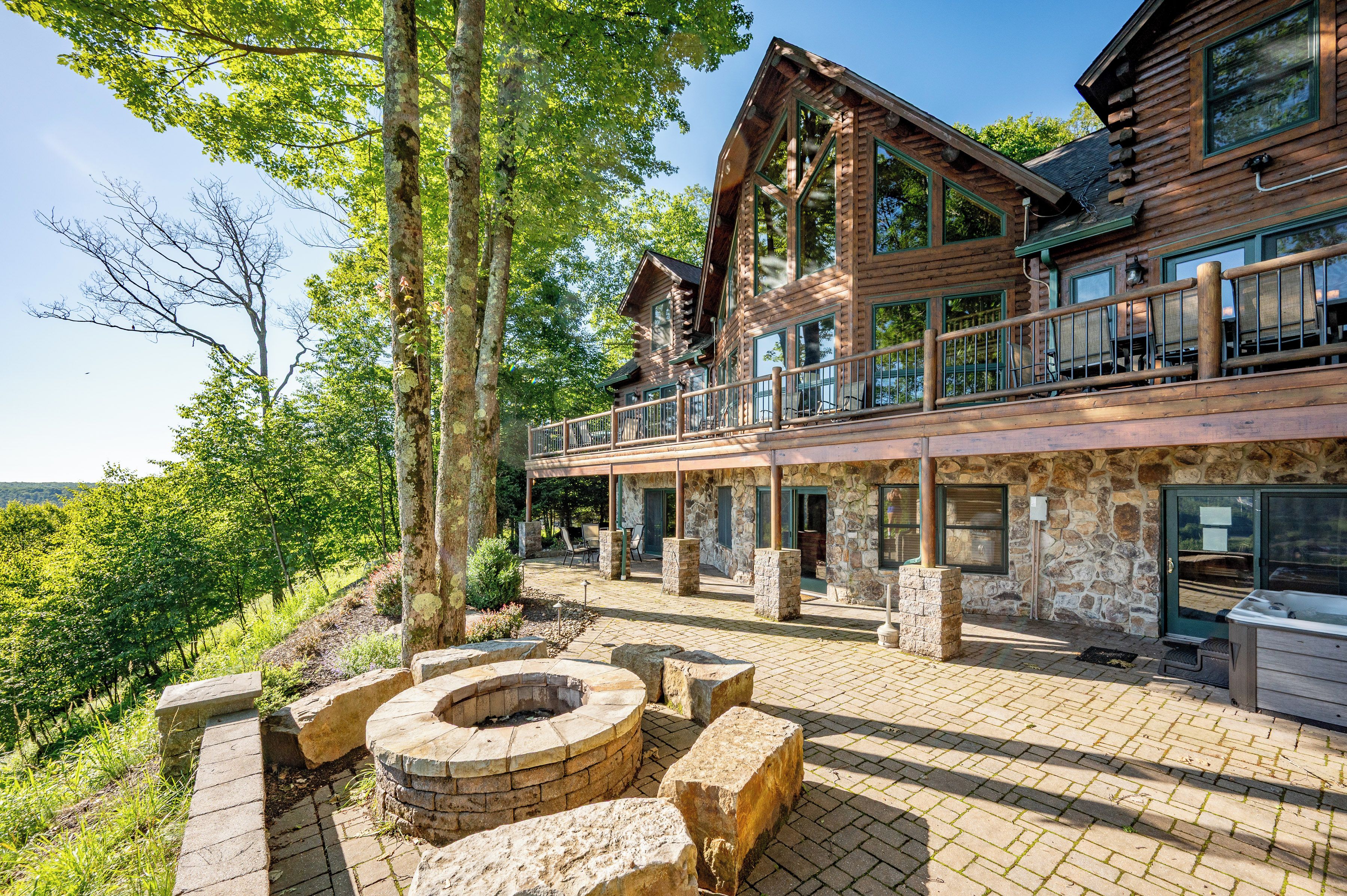 Une cabane en rondins avec des fondations en pierre, un balcon doté d’un espace salon extérieur et un foyer.
