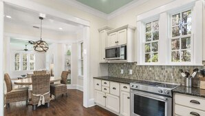 A kitchen with white cabinets, a microwave, an oven, and a dining area with wicker chairs.