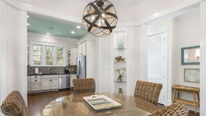 A dining area with a round glass table, wicker chairs, and a modern chandelier.