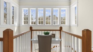 A room with a glass table, a chair, a potted plant, and a view of a house through large windows.