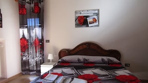 A bedroom with a bed, a nightstand, a wall-mounted photo, and a window with curtains. - B&B Dolce Dormire (Foggia)
