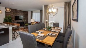 Un espace de salle à manger moderne, avec une table en bois, des chaises à revêtement gris et un lustre.