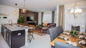 Une cuisine moderne avec un îlot central, un coin repas comprenant une table et des chaises, un canapé et un téléviseur fixé au mur.