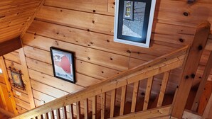 A wooden interior with a staircase, framed pictures on the walls, and a sofa with cushions. - 'Just a Step Away' - a Secluded Cabin on Stover Creek w/Fiber Wi-Fi & Hot Tub (Ellijay)