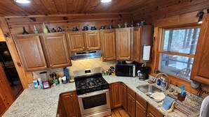A kitchen with wooden cabinets, granite countertops, a stove, oven, microwave, sink, and a window. - 'Just a Step Away' - a Secluded Cabin on Stover Creek w/Fiber Wi-Fi & Hot Tub (Ellijay)