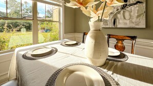 Une salle à manger avec une table mise pour quatre personnes, un vase rempli de fleurs et un tableau accroché au mur.