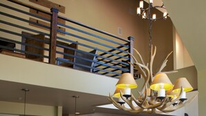 Un vaste espace de vie doté d’un haut plafond, une table à manger avec des chaises, un escalier et une cuisine en arrière-plan.