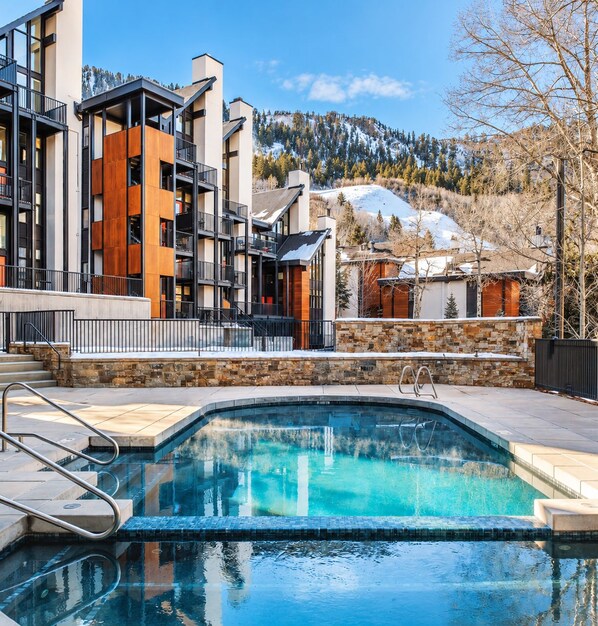 A modern hotel with a pool, stone walls, and a view of snow-capped mountains.