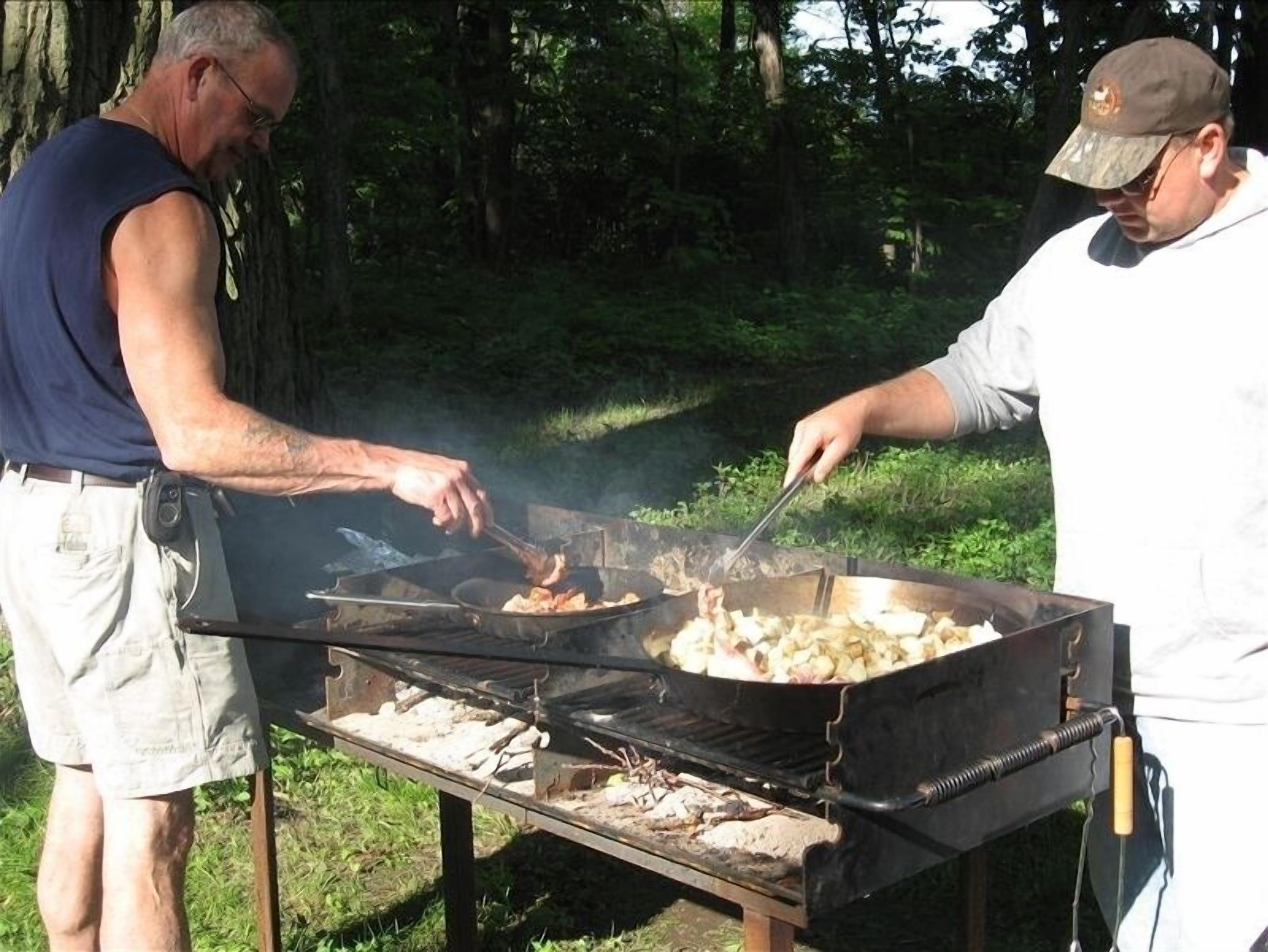 Två personer grillar utomhus med en portabel grill.
