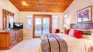 Een slaapkamer met een groot bed, houten hoofdbord, een televisie, een dressoir en een glazen schuifdeur naar een balkon.