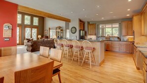 Een ruime keuken met houten kasten, een eethoek met een houten tafel en stoelen, en een groot kookeiland met barstoelen.