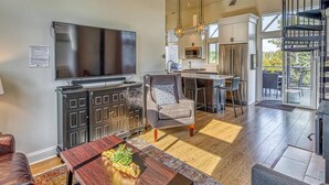 A modern living room with a flat-screen TV, a dark wooden cabinet, a grey sofa, and a dining table with a decorative centerpiece. - Smart Home, direct Beach Dunes Nat’l Park access, Hot Tub, luxury amenities (Miller Beach)