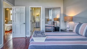 A bedroom with a large bed, a bedside table with a lamp, and a mirror. There is a door leading to another room. - Smart Home, direct Beach Dunes Nat’l Park access, Hot Tub, luxury amenities (Miller Beach)