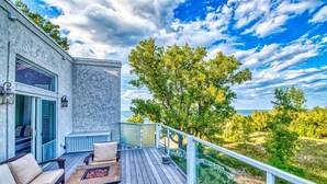 A deck with outdoor furniture, a view of the ocean, and a building with a stone facade. - Smart Home, direct Beach Dunes Nat’l Park access, Hot Tub, luxury amenities (Miller Beach)