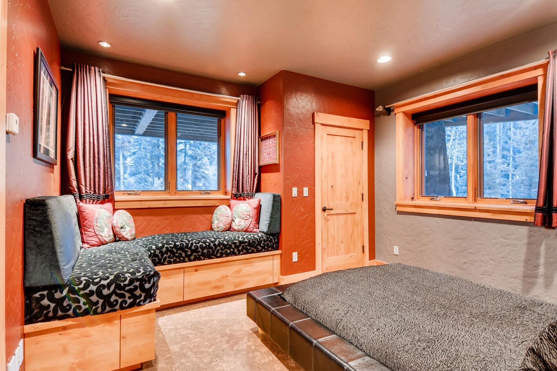 A cozy room with a bed, a bench with cushions, and two windows with curtains.