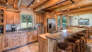 A spacious kitchen with wooden cabinets, a large island with stools, stainless steel appliances, and a view of the outdoors. - Beautiful Secluded Log Home 5 minutes from town. (Hamilton)