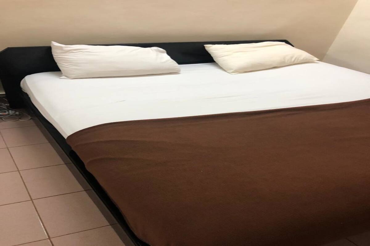 A bed with a white mattress and two pillows, a brown blanket, and a black headboard.
