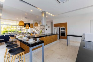 A modern kitchen with a central island, bar stools, stainless steel appliances, and large windows. - Marina Vallarta Garden House | Ocean & Pool Vibe (Puerto Vallarta)