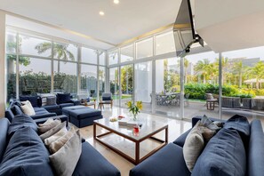 A modern living room with a large glass wall, a sofa set, a coffee table, and a dining area visible through the glass. - Marina Vallarta Garden House | Ocean & Pool Vibe (Puerto Vallarta)