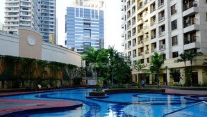 A swimming pool with a blue and red design, surrounded by greenery and modern buildings in the background. - Forbeswood Heights 2BR by Stays PH (Taguig)