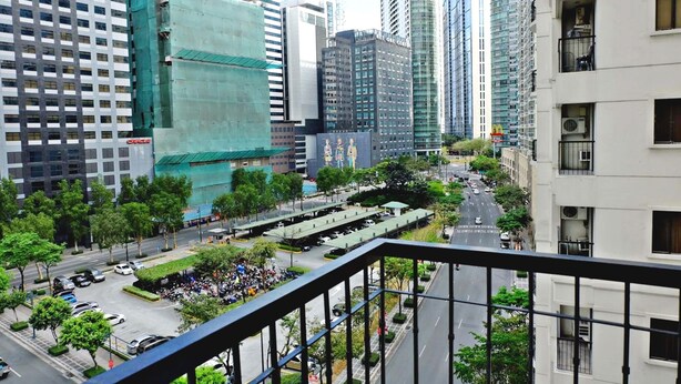 A cityscape with high-rise buildings, a parking lot, and a group of people gathered in a park area. - Forbeswood Heights 2BR by Stays PH (Taguig)