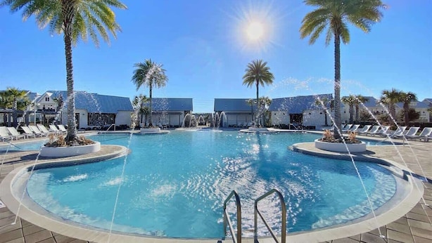 A swimming pool with lounge chairs and palm trees, surrounded by buildings.