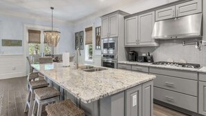 A kitchen with a large island, stainless steel appliances, and a hanging light fixture.