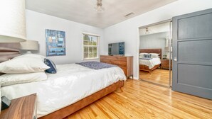 A bedroom with a wooden floor, a bed with white bedding, a dresser, a television, and a mirror on the wall. - City Haven (Burbank)
