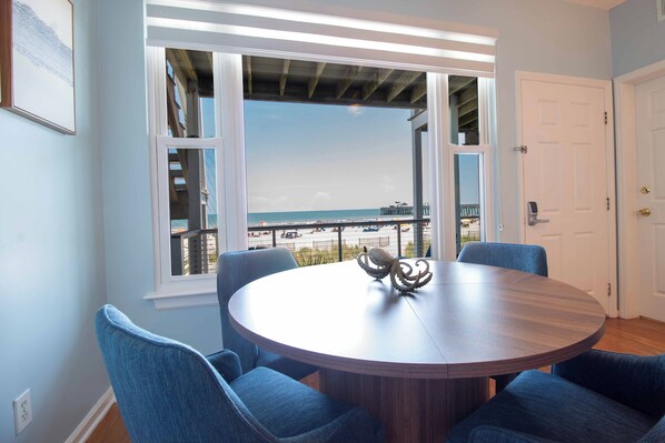 A round wooden table with four blue chairs, a decorative octopus sculpture, and a view of the ocean through a large window.