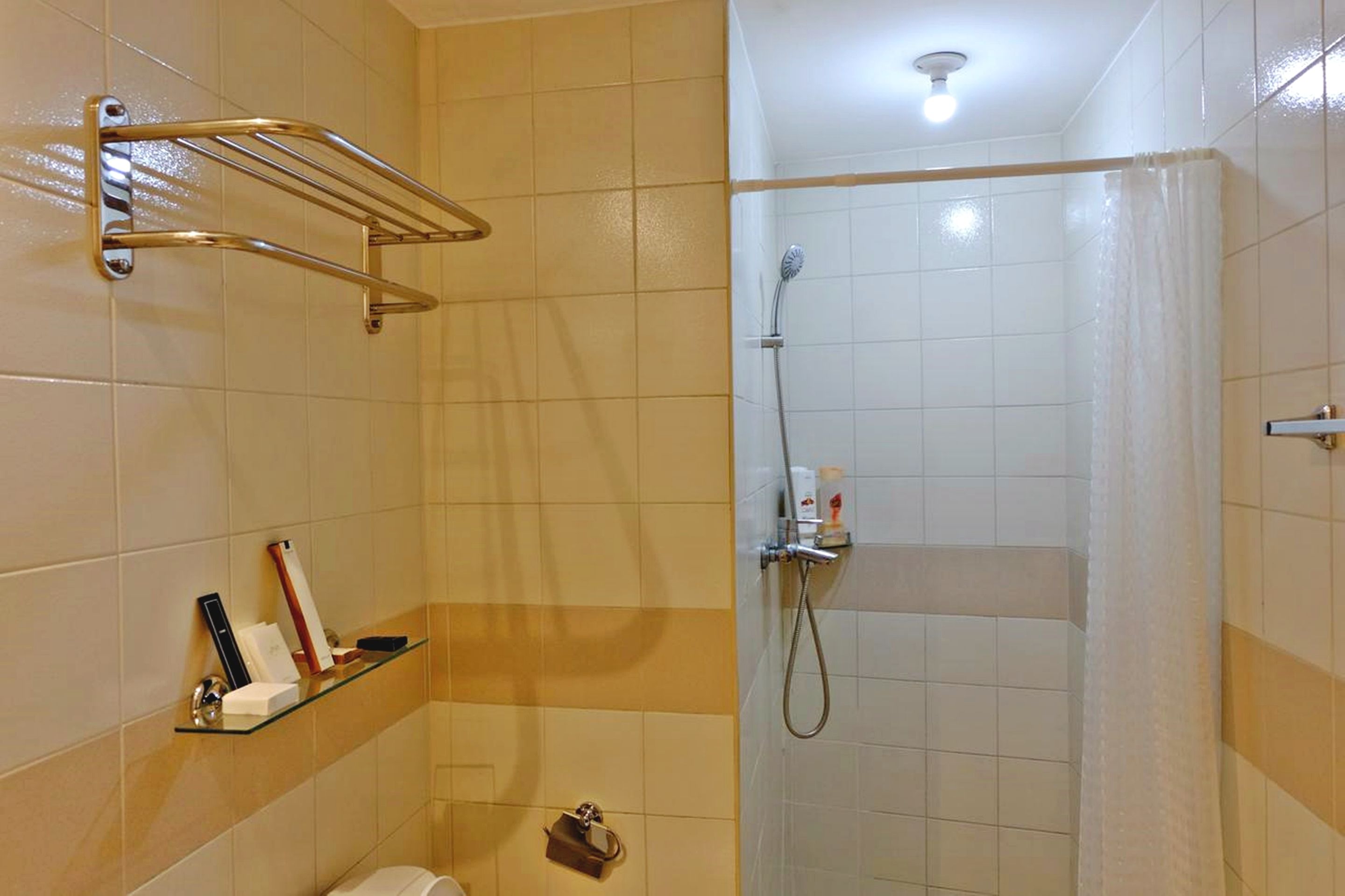 A bathroom with a shower, a towel rack, and a shelf with toiletries.