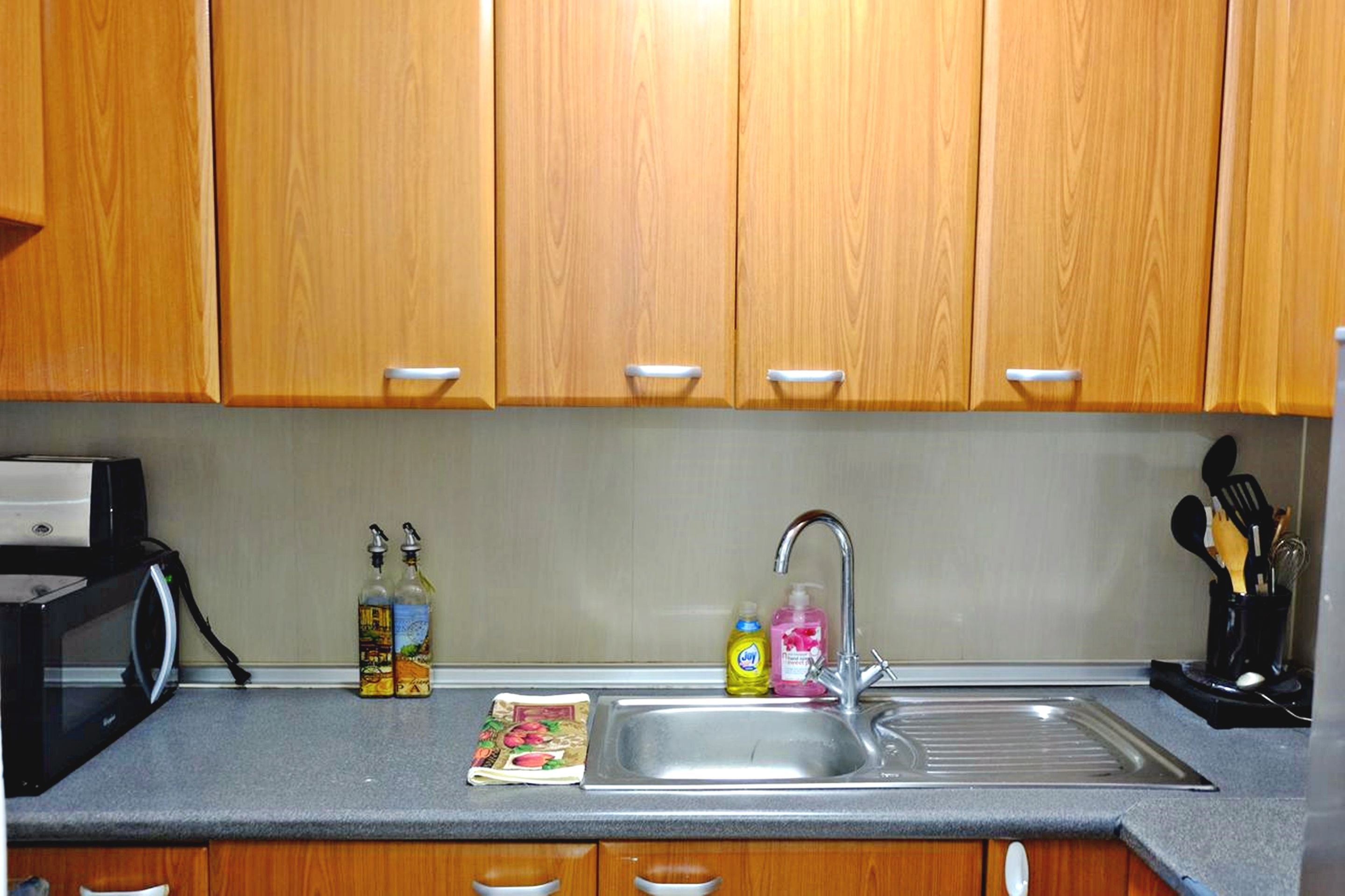 A kitchen with wooden cabinets, a stainless steel sink, and various kitchen items like bottles and a microwave.