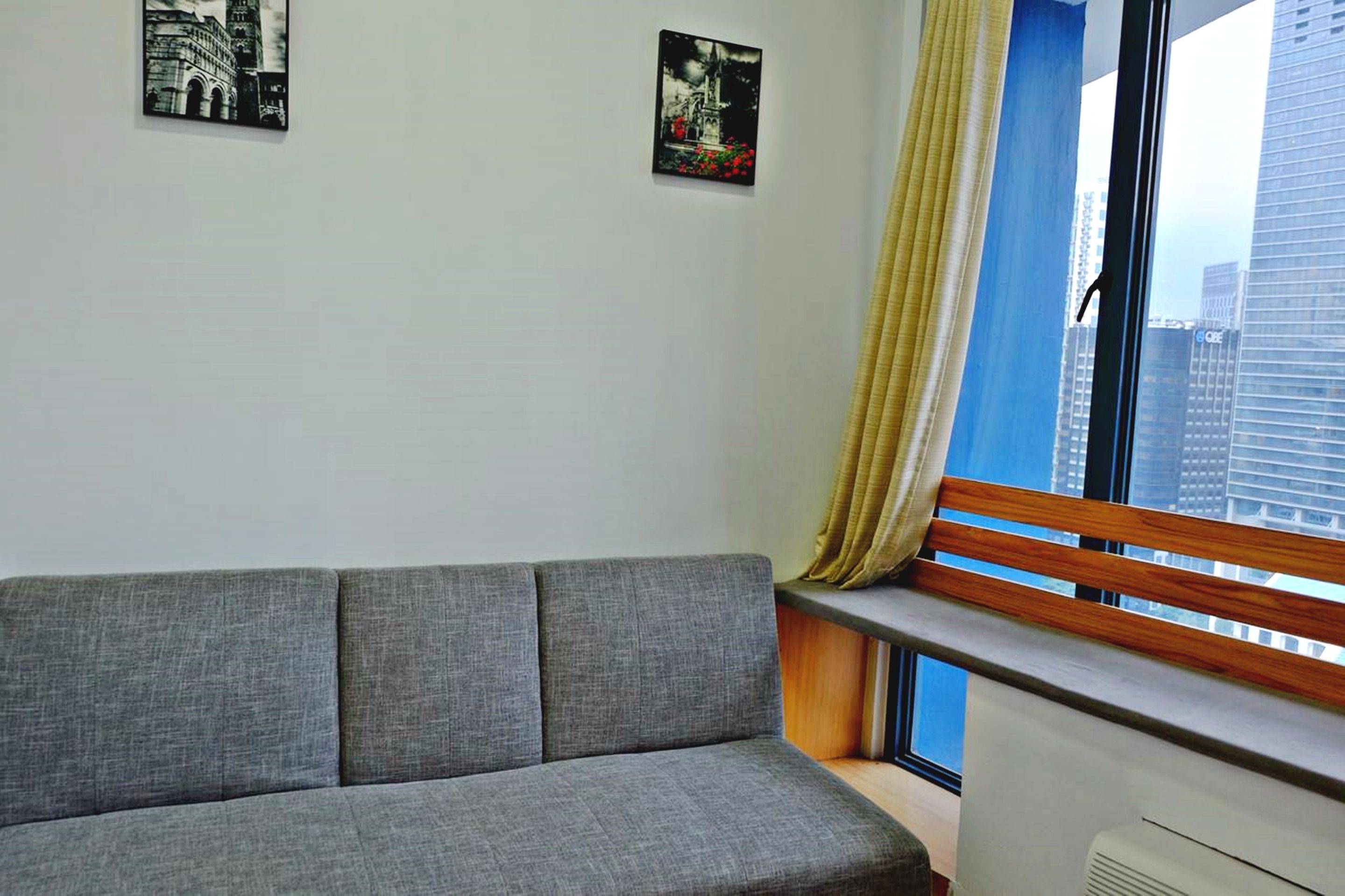 Un salón moderno con un sofá gris, una ventana con marco de madera y dos cuadros en blanco y negro colgados en la pared.