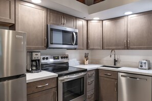 A modern kitchen with stainless steel appliances, wooden cabinets, a built-in oven, and a coffee maker. - Aspenwood L3 - Ski, Soak, Relax | Cozy Mountain Stay, Walk to Slopes (Snowmass Village)