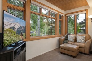 A room with a large window, a flat-screen TV, a leather sofa, and a carpeted floor. - Aspenwood L3 - Ski, Soak, Relax | Cozy Mountain Stay, Walk to Slopes (Snowmass Village)