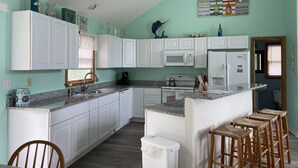 A kitchen with white cabinets, a granite countertop, and a small island with stools. There is a microwave, stove, and refrigerator. - Beach Oasis. 2 Mins to Priv Beach&4X4 beach.Hottub.Foosball.Close to shop/dining (Corolla)