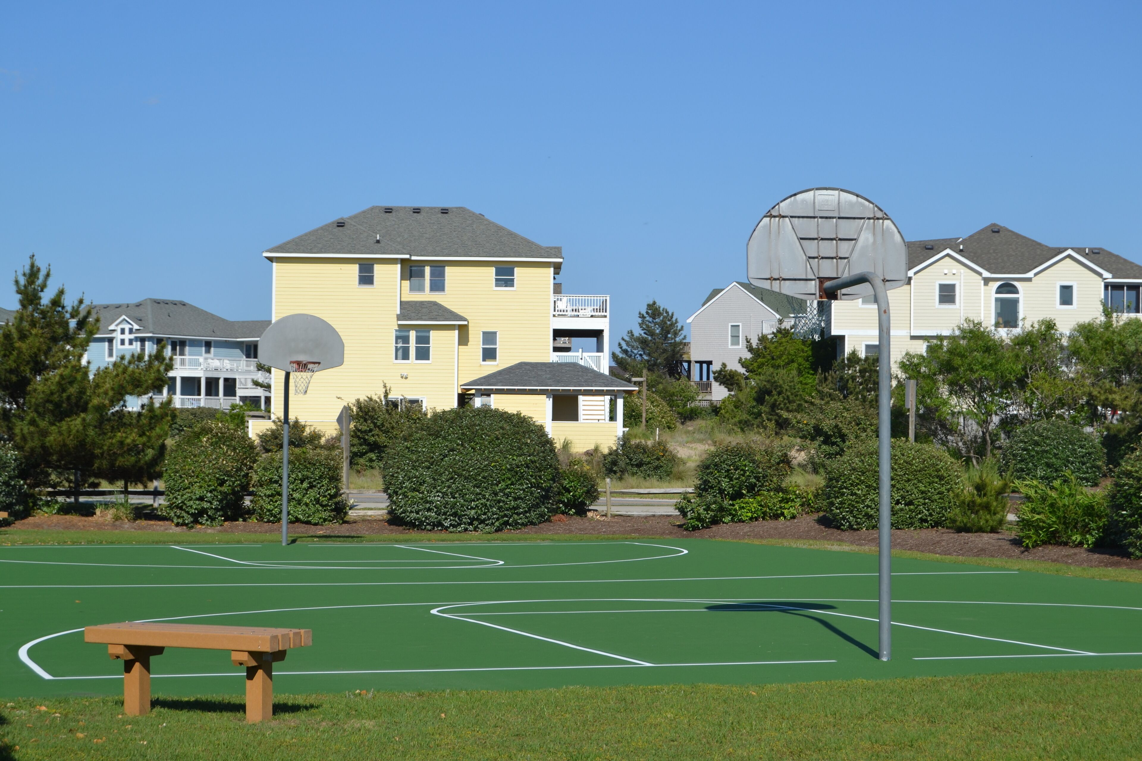 A basketball court with a bench, surrounded by houses and greenery.