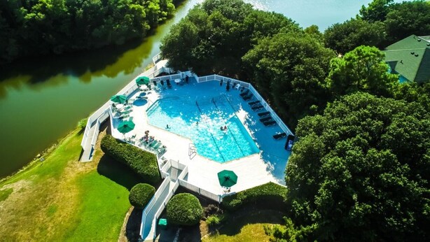 An aerial view of a swimming pool surrounded by lush greenery and a body of water. - Beach Oasis. 2 Mins to Priv Beach&4X4 beach.Hottub.Foosball.Close to shop/dining (Corolla)
